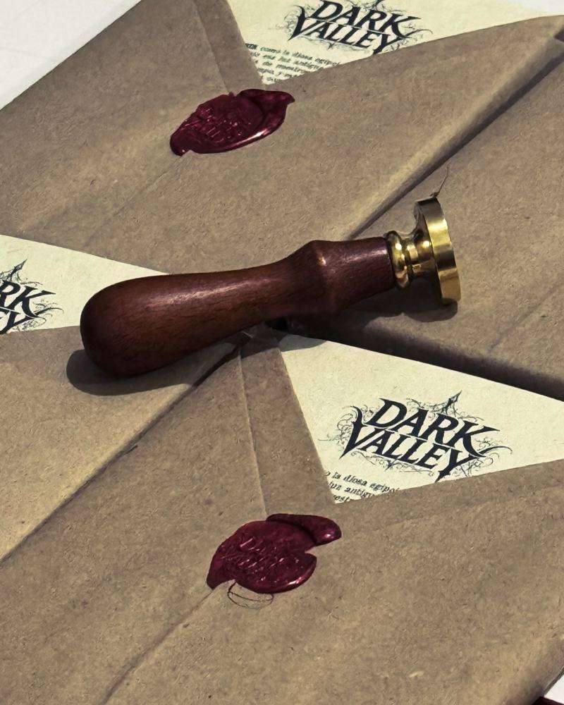 Sobres de papel kraft sellados con lacre rojo y el sello de latón con mango de madera, con la carta de Dark Valley asomando